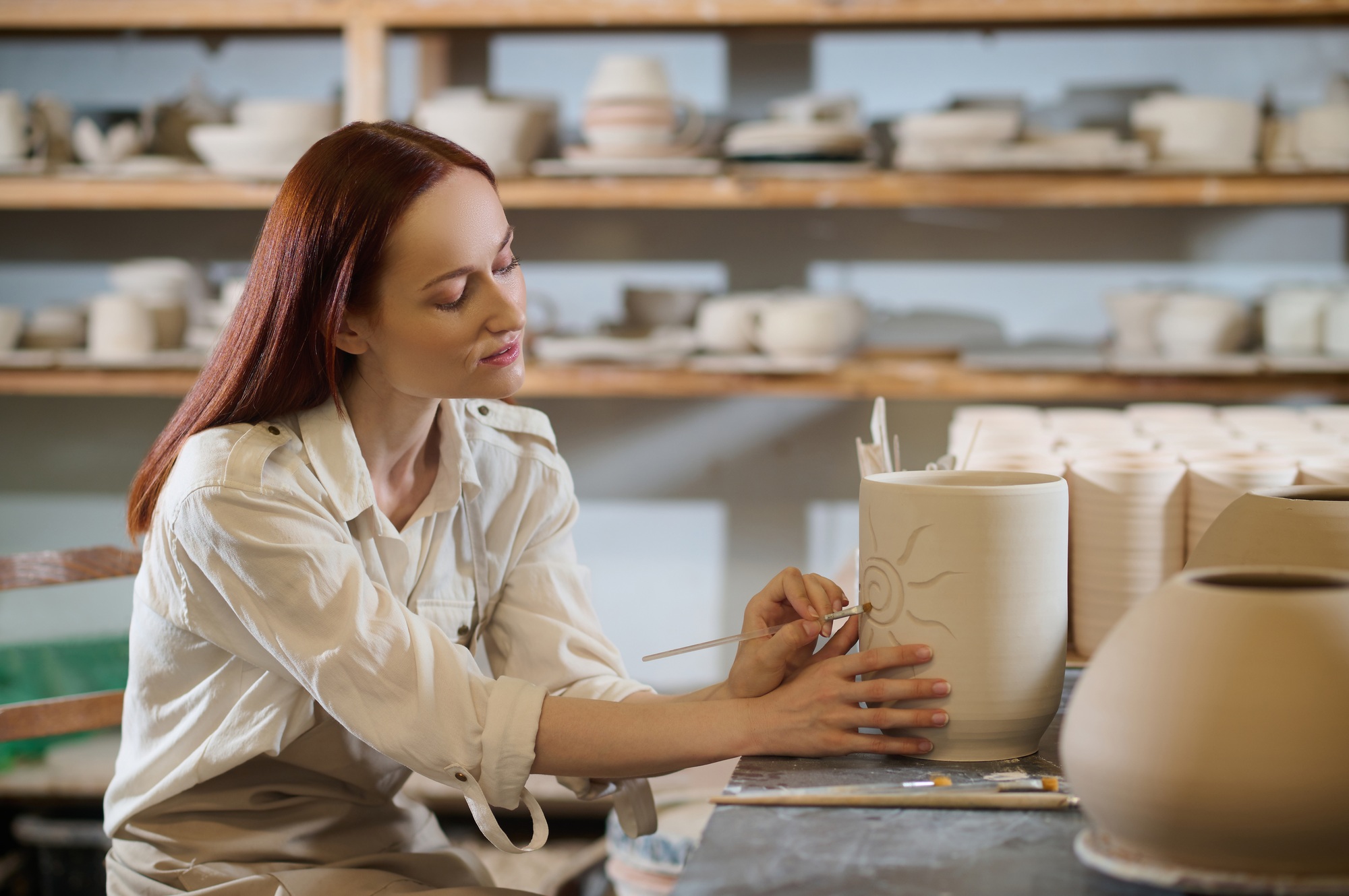 A pretty woman looking involved while painting the pot