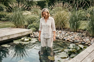 Femme se baignant dans une piscine naturelle entourée de plantes aquatiques et de pierres dans un jardin écologique